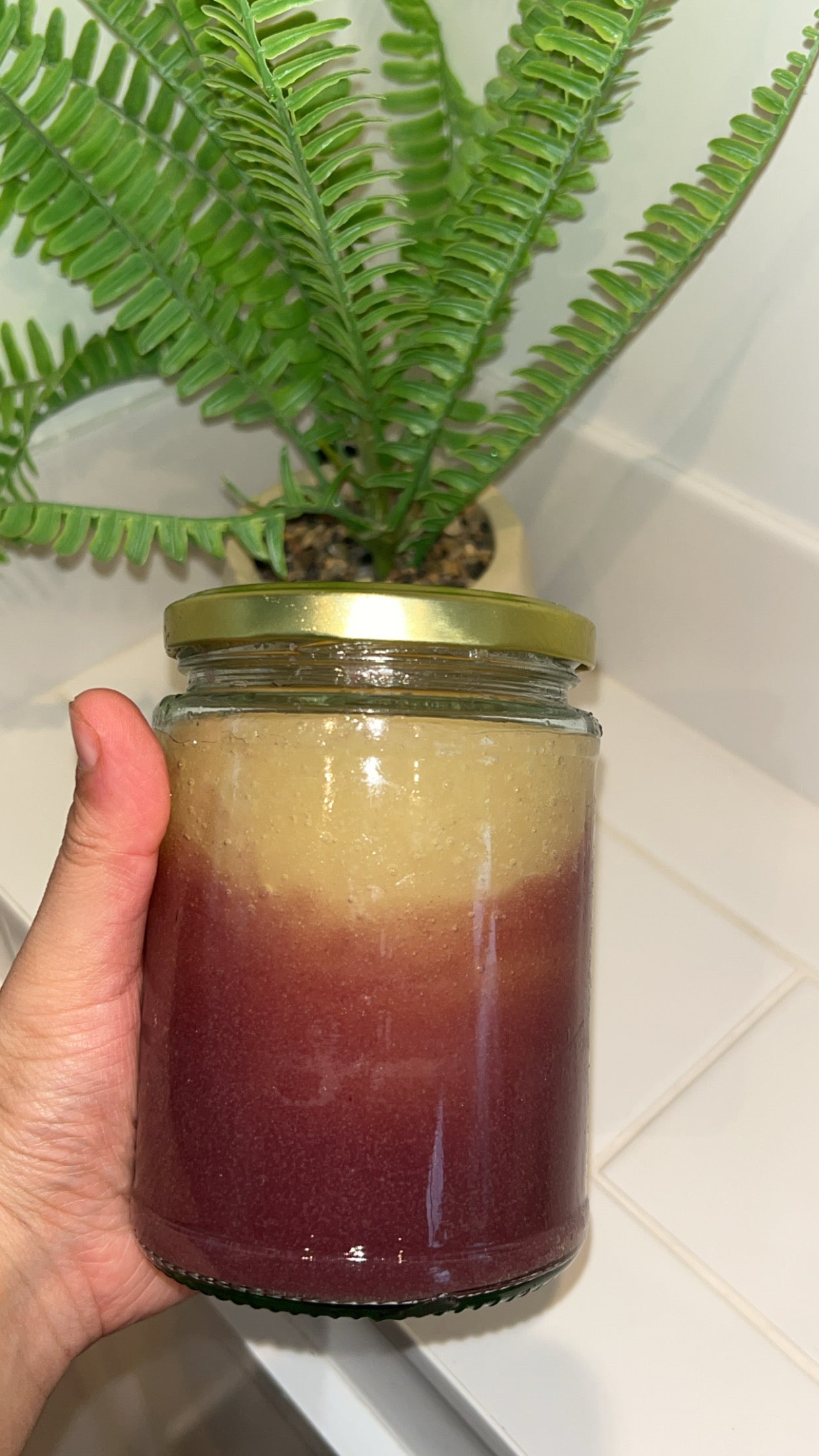 500ml Organic Purple and Gold Sea Moss gel. Front shot. Lady holding it in her hand behind a plant